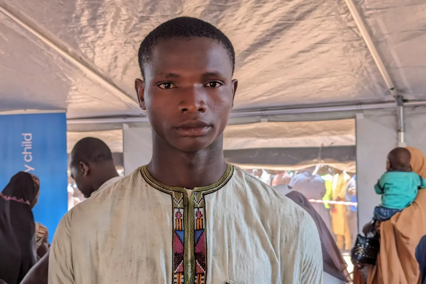 A young man is standing in an internally displaced persons (IDP) camp.