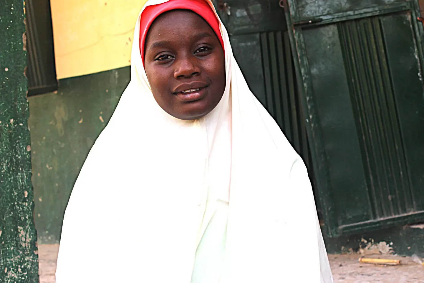 A young girl in white hijab standing in front of a classroom. 