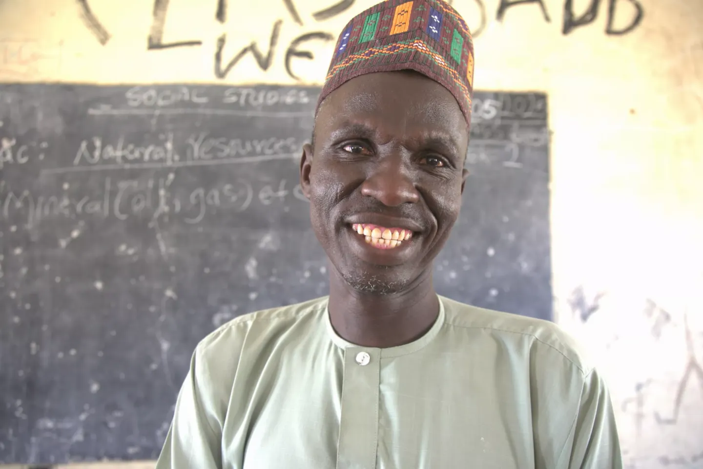 A man with a smiling face is standing in front of the chalkboard.