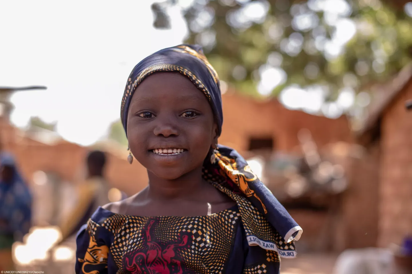 A child smiling in front of her house. 