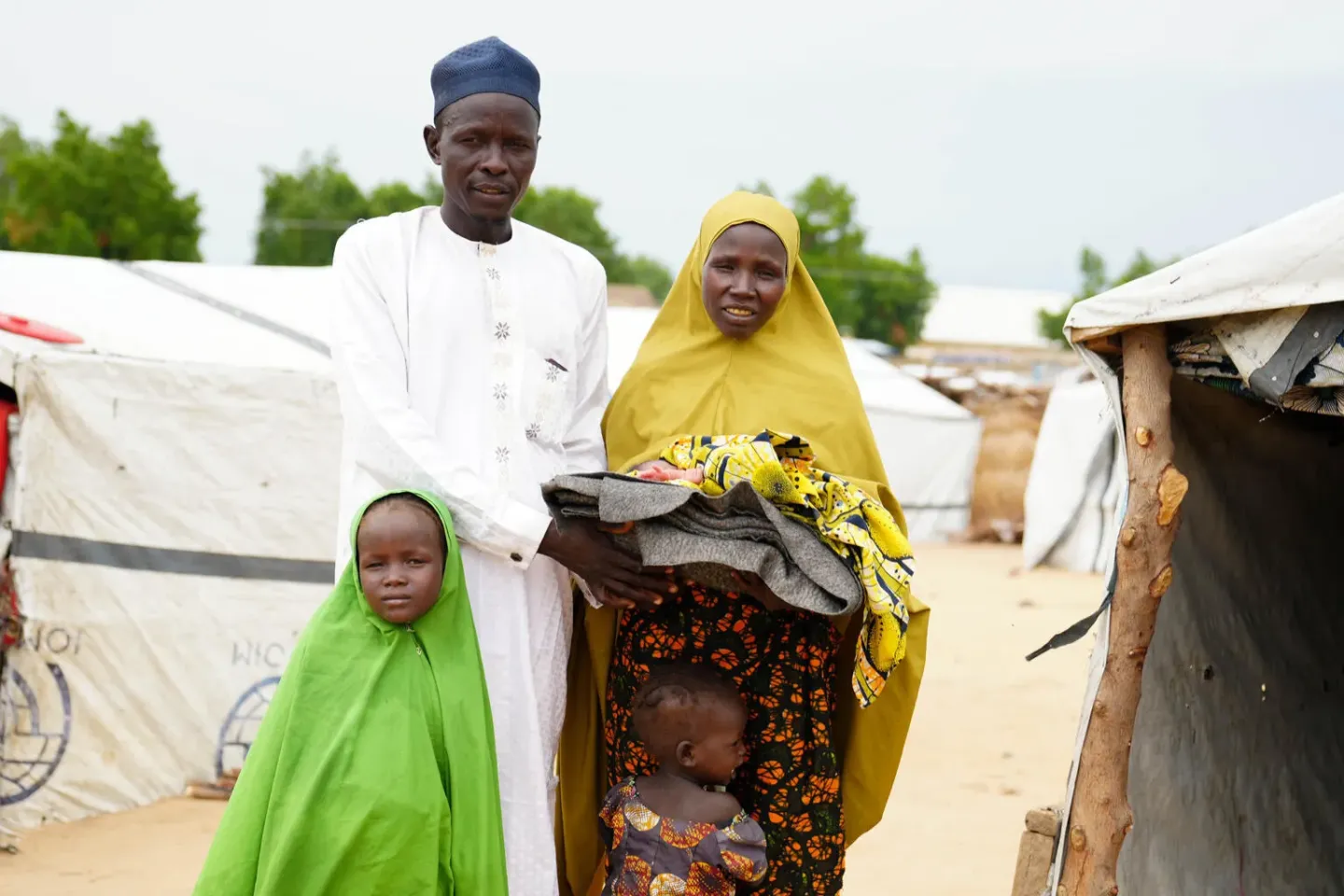 Portrait of Mallam Ali, a member of the Engaging Men through Accountable Practice (EMAP) group, with his wife and newborn child, in New Camp, Bama, Borno State.