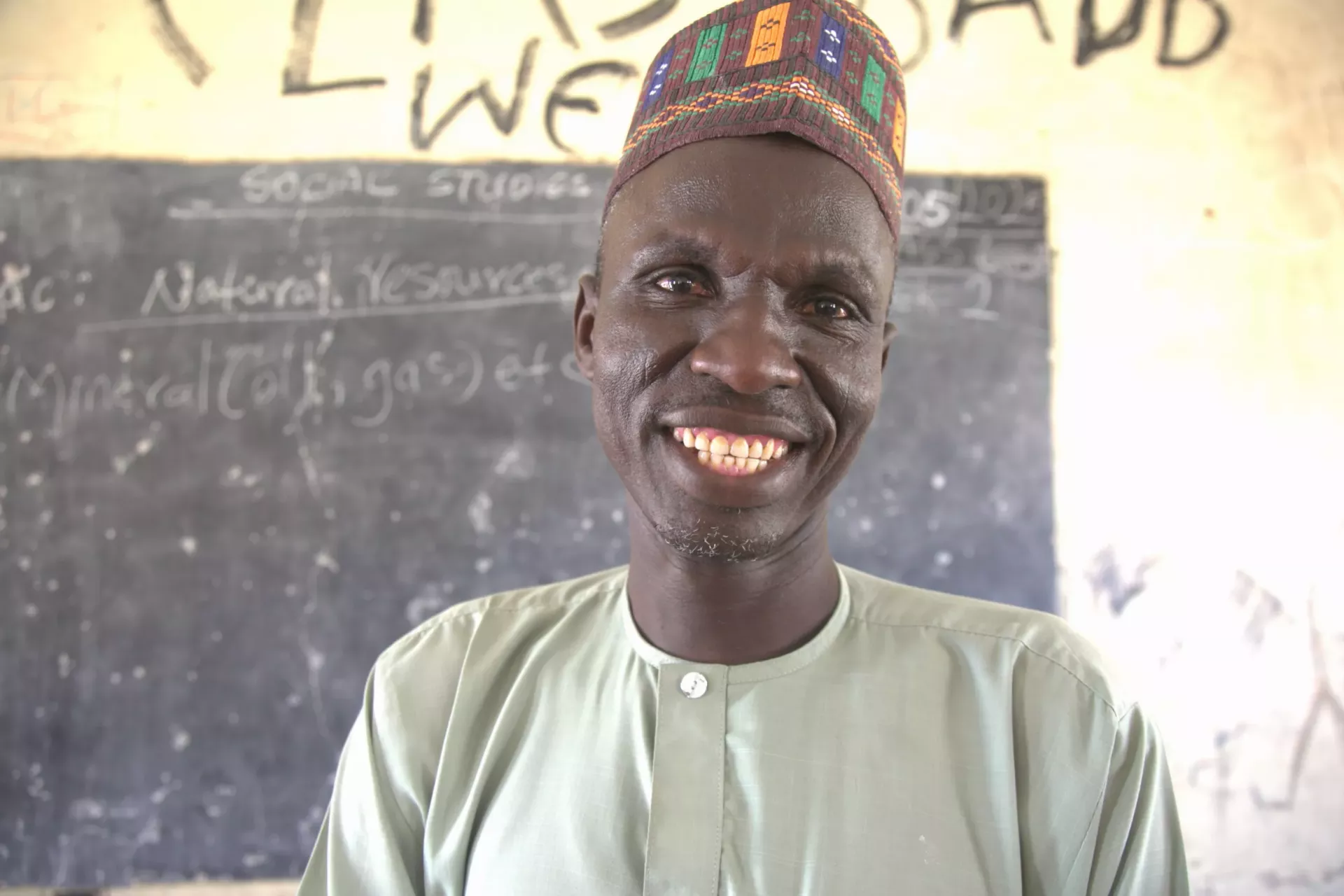 A man with a smiling face is standing in front of the chalkboard.