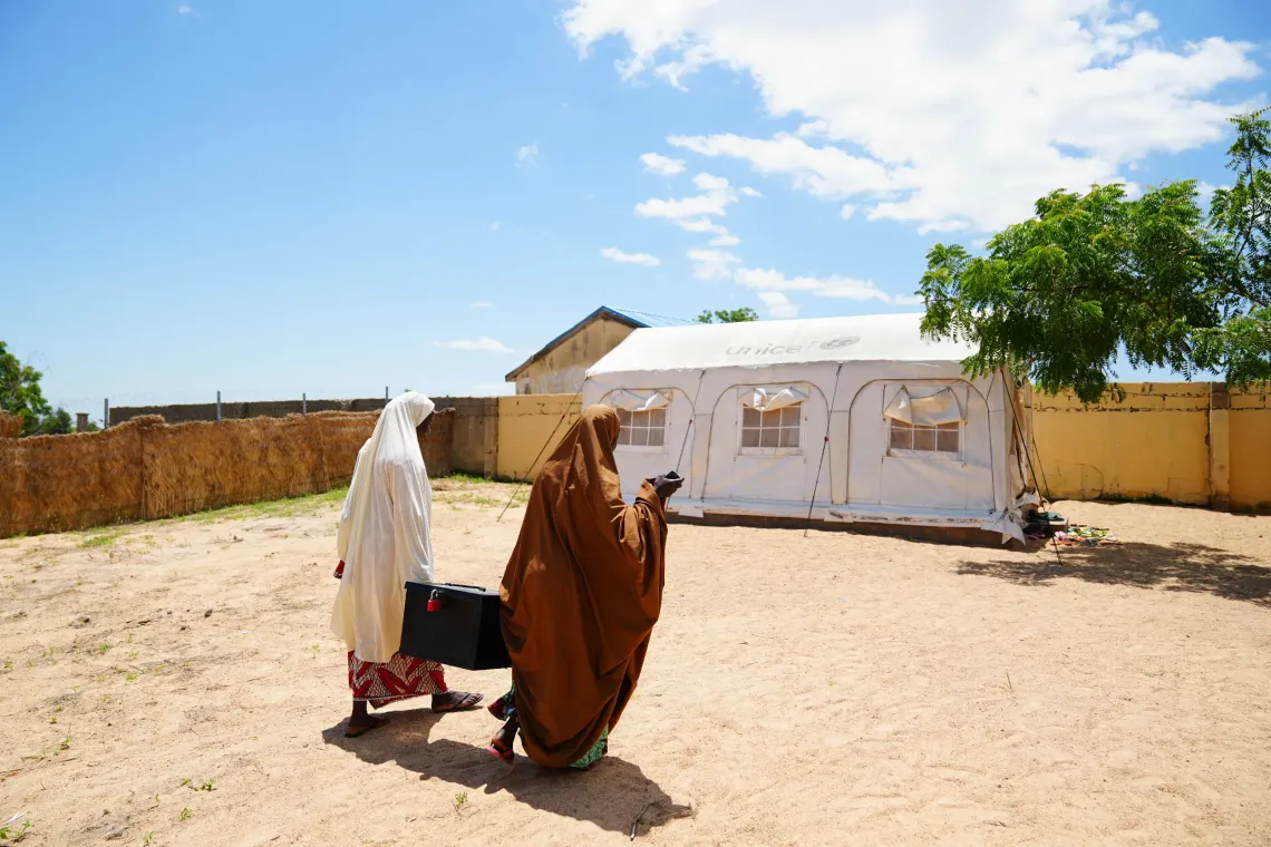 Women carrying a savings box to the tent