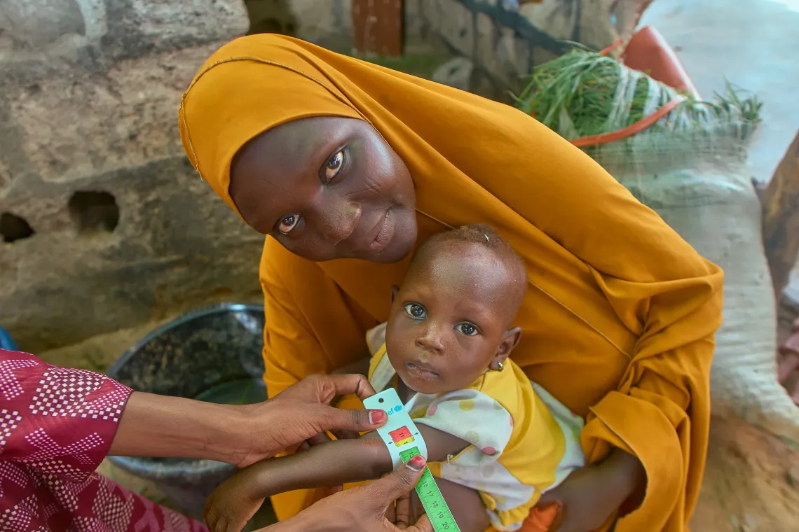 Shamsiyya Isiyaku, 30, sits with her 1-year-old daughter, Ummusalama Rabiu, as local community volunteer Rahama Aliyu screens the child during a house-to-house visit in Bayan Hayin Gada Ward, Jibia.