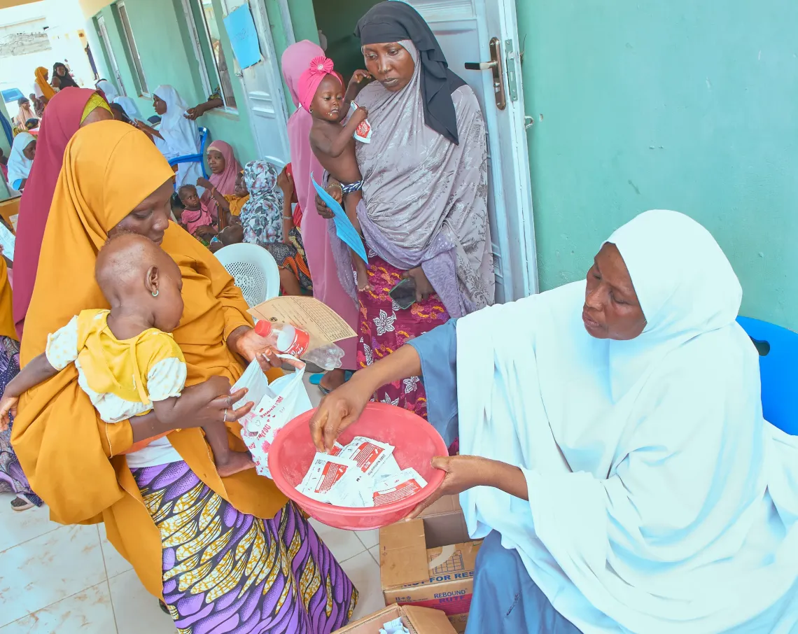 A health worker hands 14 sachets of Ready-to-Use Therapeutic Food (RUTF) to Shamsiyya Isiyaku, 30, for her 1-year-old daughter, Ummusalama Rabiu, at the Jibia Babba Primary Healthcare Centre in Jibia.