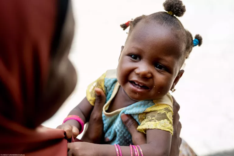 11 months old Fatimah smiles in the arms of her mother, Hasiya