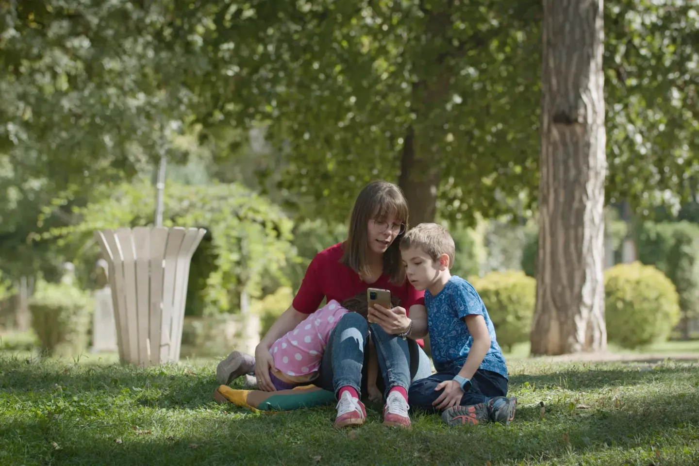 Mother and her children sitting in a park looking at the phone for ideas for play
