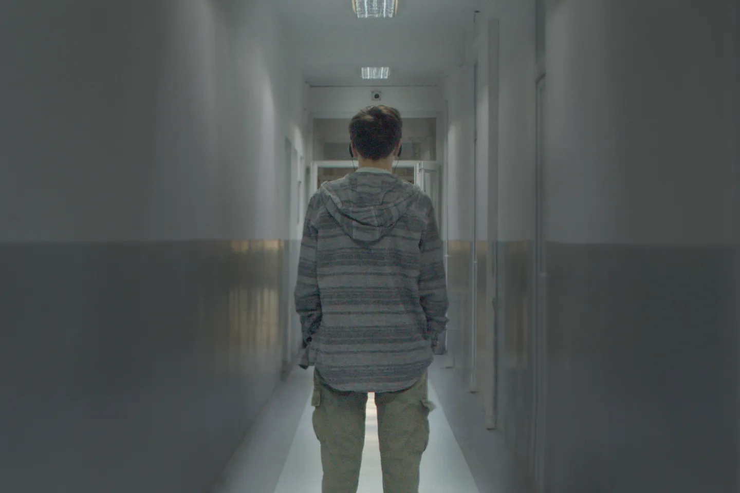 Adolescent boy facing back walking down a narrow corridor, picture with foggy effect