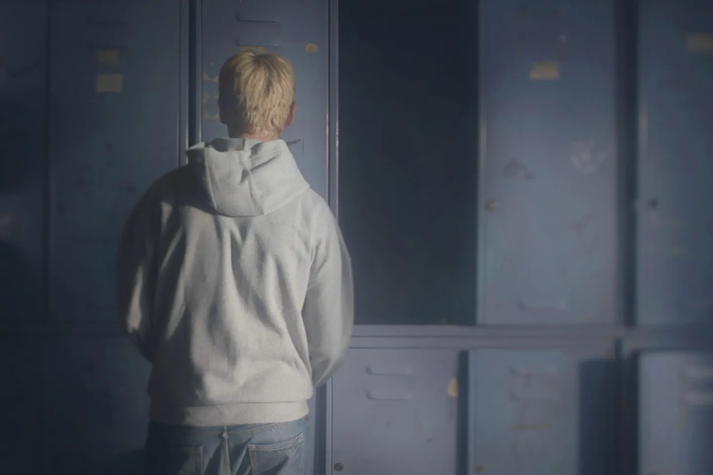 Adolescent boy facing back looking at gray lockers
