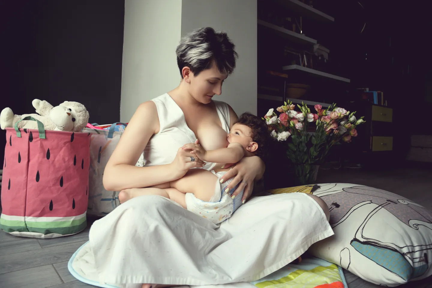 Mother in white dress sitting on the floor breastfeeding her child