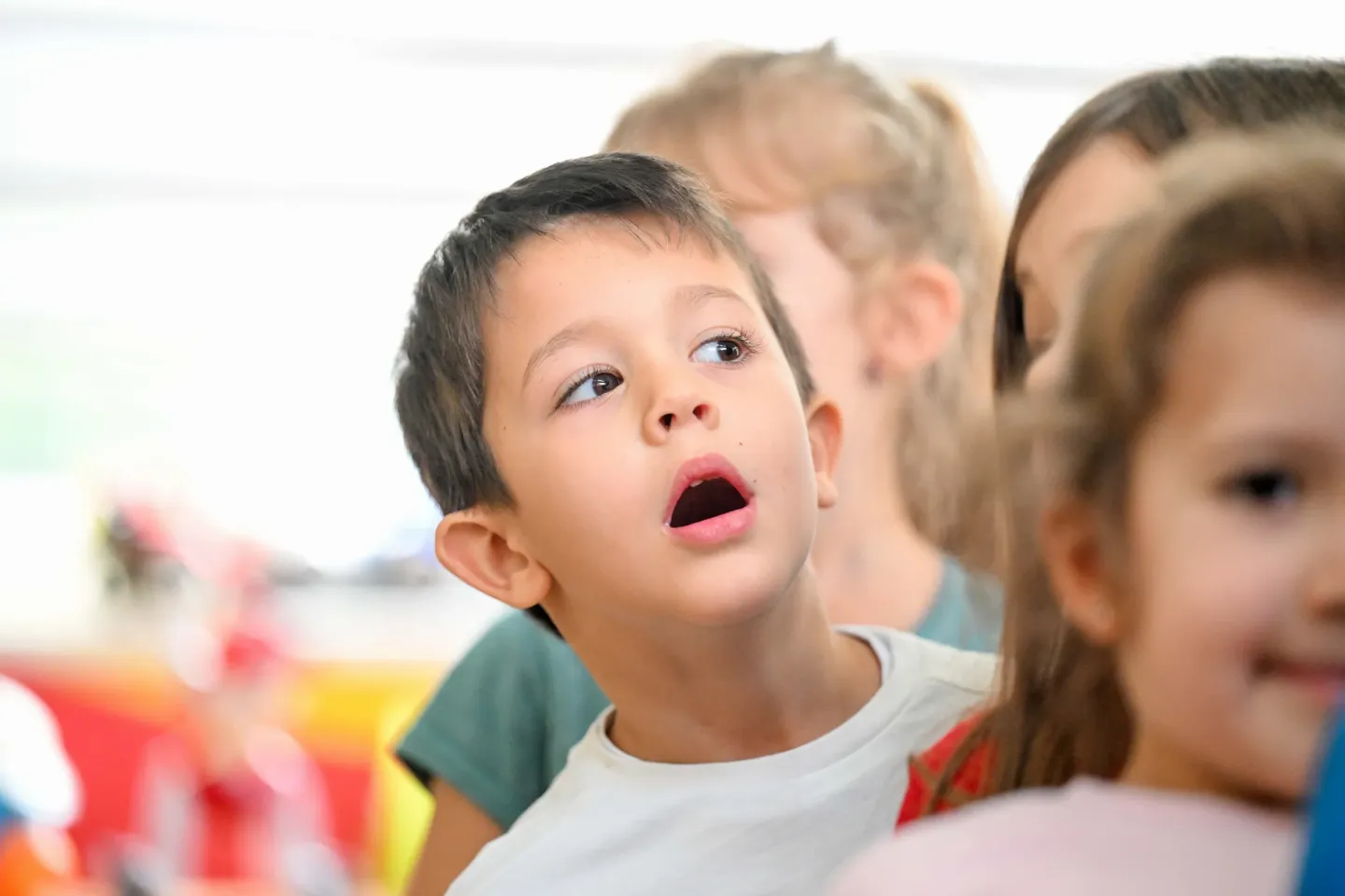 Boy in kindergarten standing between his friends, looking curiously and attentively 