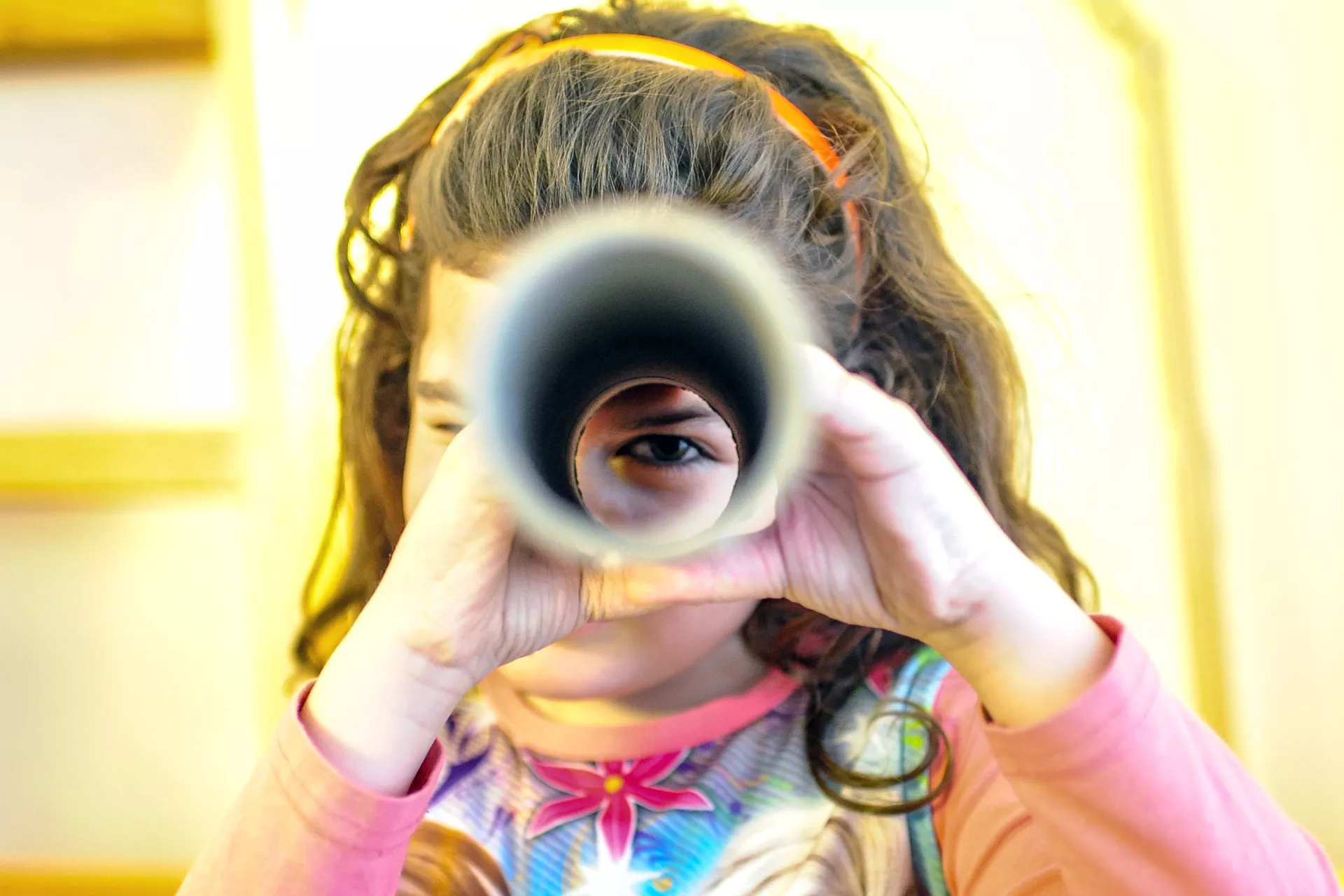 A girl looks through a rolled paper 