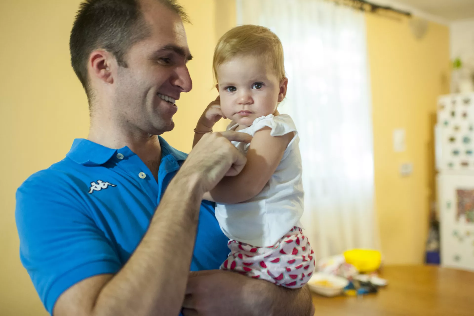 Man in a blue t-shirt smiling and holding a baby 
