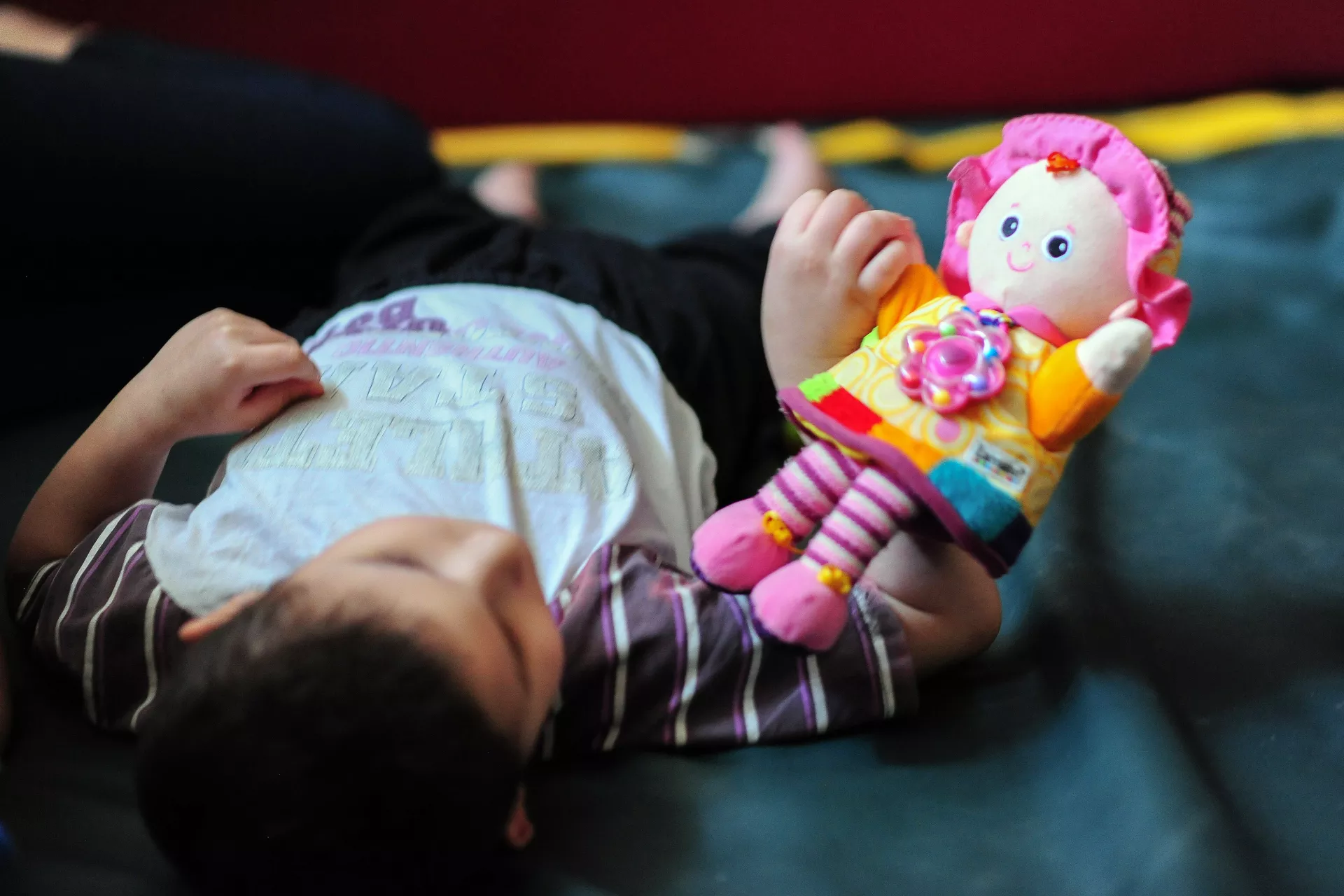 A child laying on the floor is looking at a doll that he holds in his right hand
