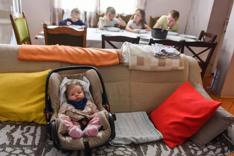 A baby on a couch in the foreground, 4 kids around the dining table in the background 