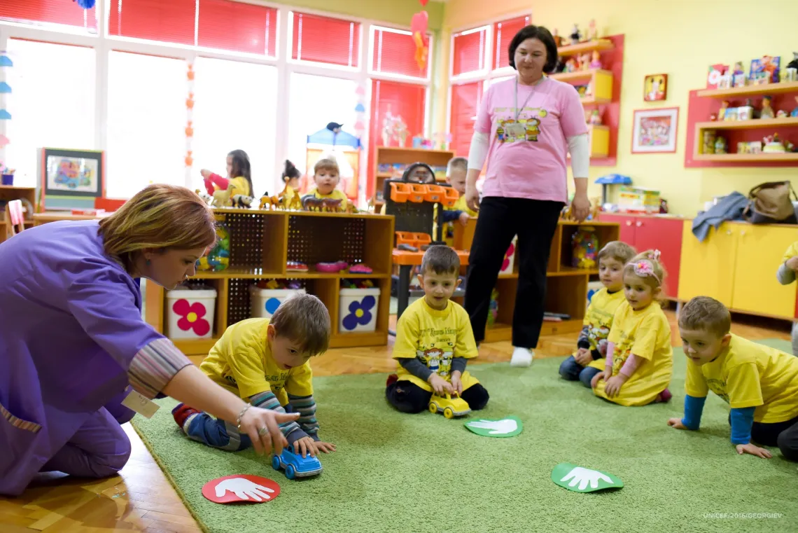 Children sitting on the floor in a kindergarten, while Mihail (4 years old) who has cerebral palsy plays with a blue toy car