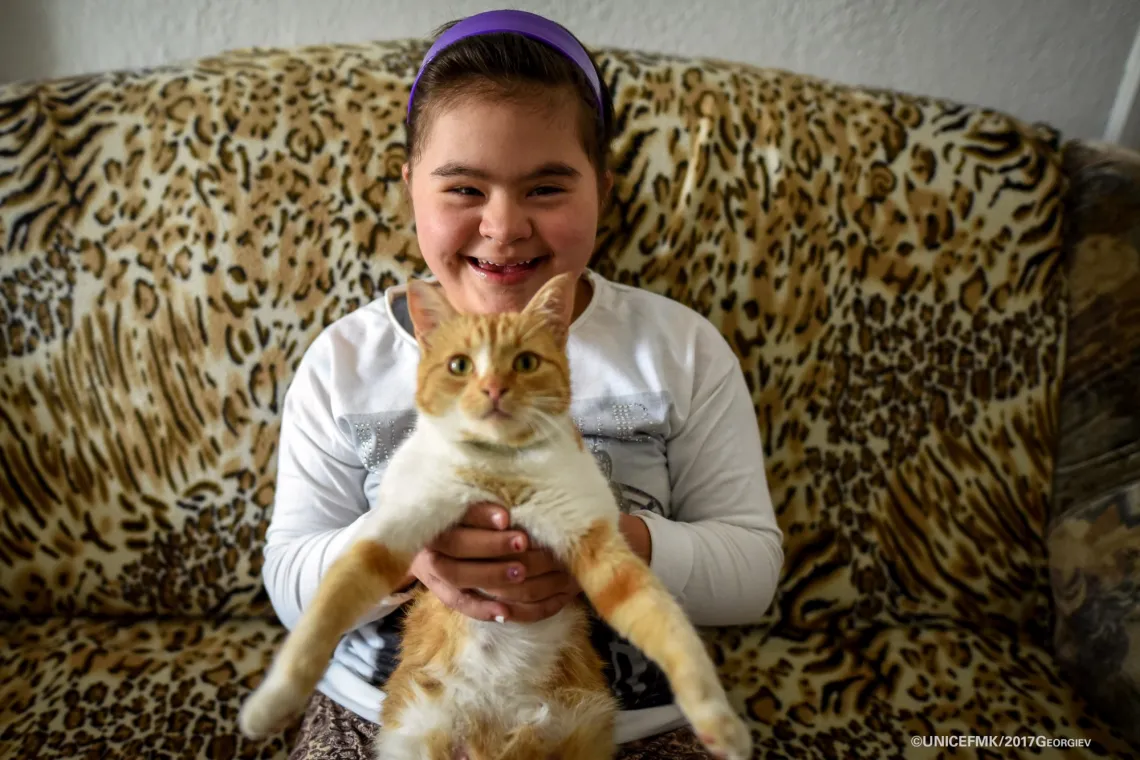 12 year old Stefanija who has down syndrome holds her cat on the couch in the living room of her family house in Delcevo