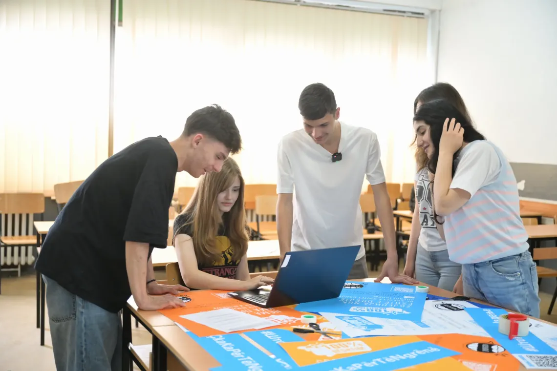 Group of adolescents looking at a laptop and working on posters with data and messages on food environments in their school