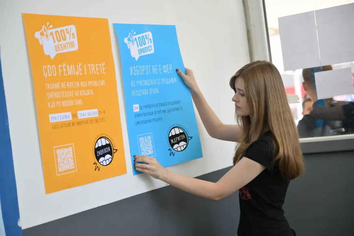 An adolescent girl placing a poster with messages and data on food environment in schools in the hallway