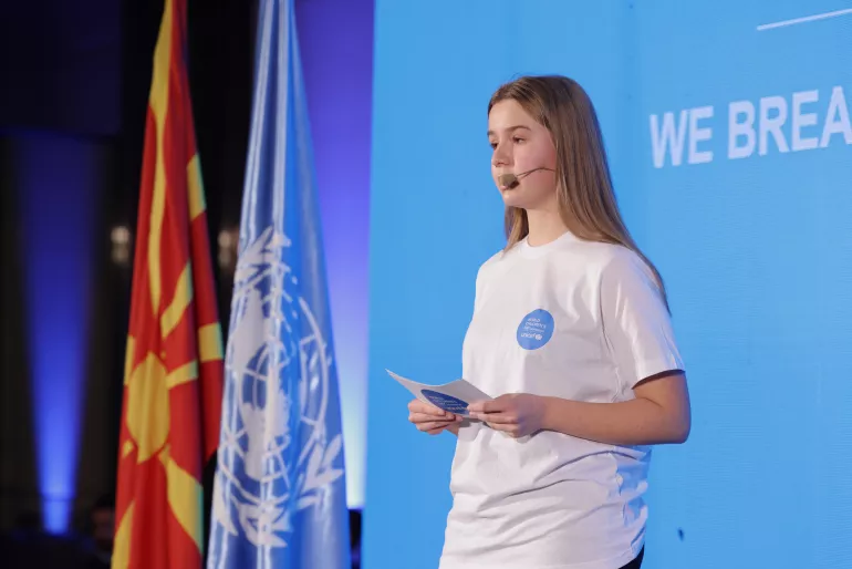 Girl wearing white t-shirt giving speech on stage at World Children's Day event 