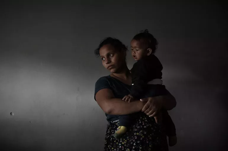 Pregnant mother cradling her one-year-old son in their home in Gazi Baba