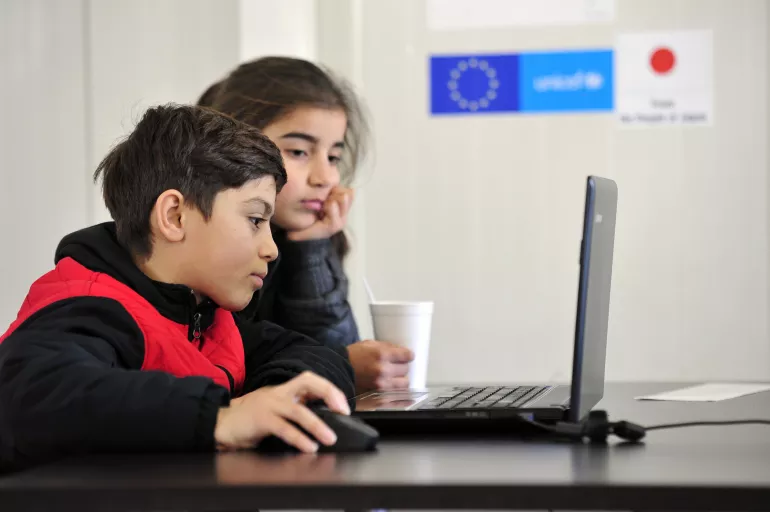 A young boy and a young girl look at a computer monitor on ICT classes organized by UNICEF at the refugee and migrant transit centre Tabanovce