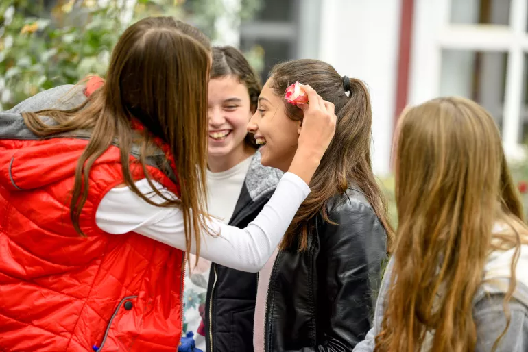 Group of girls laughing, one puts a flower in the hair of her friend smiling (UNICEF North Macedonia)