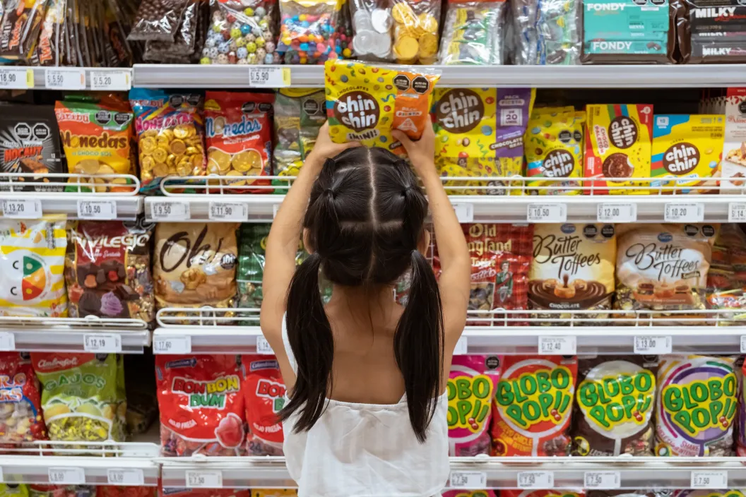 Girl takes candy from a shelf filled with ultra-processed food 