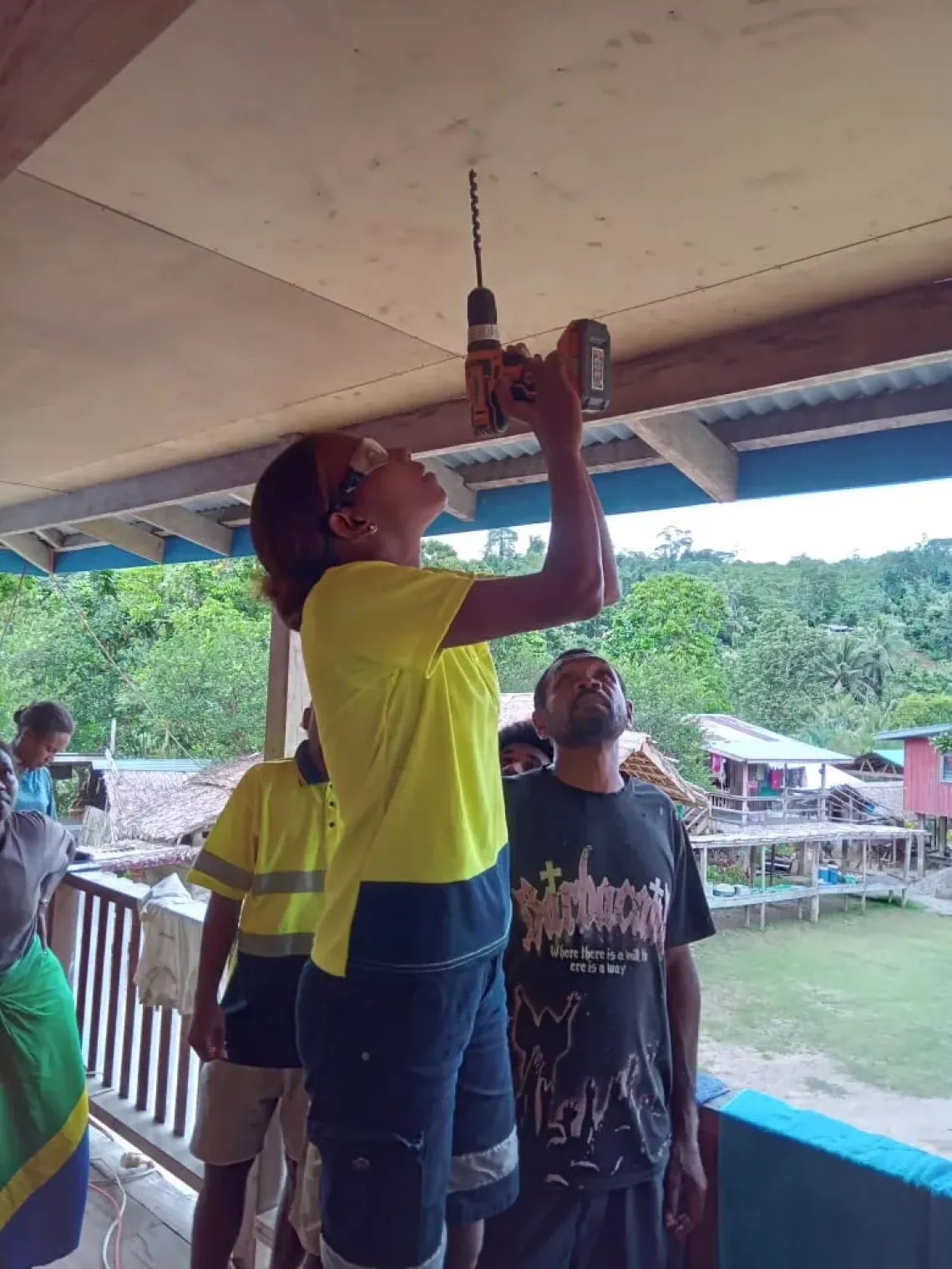 Newly trained Salica drills a hole in the ceiling to install solar power.