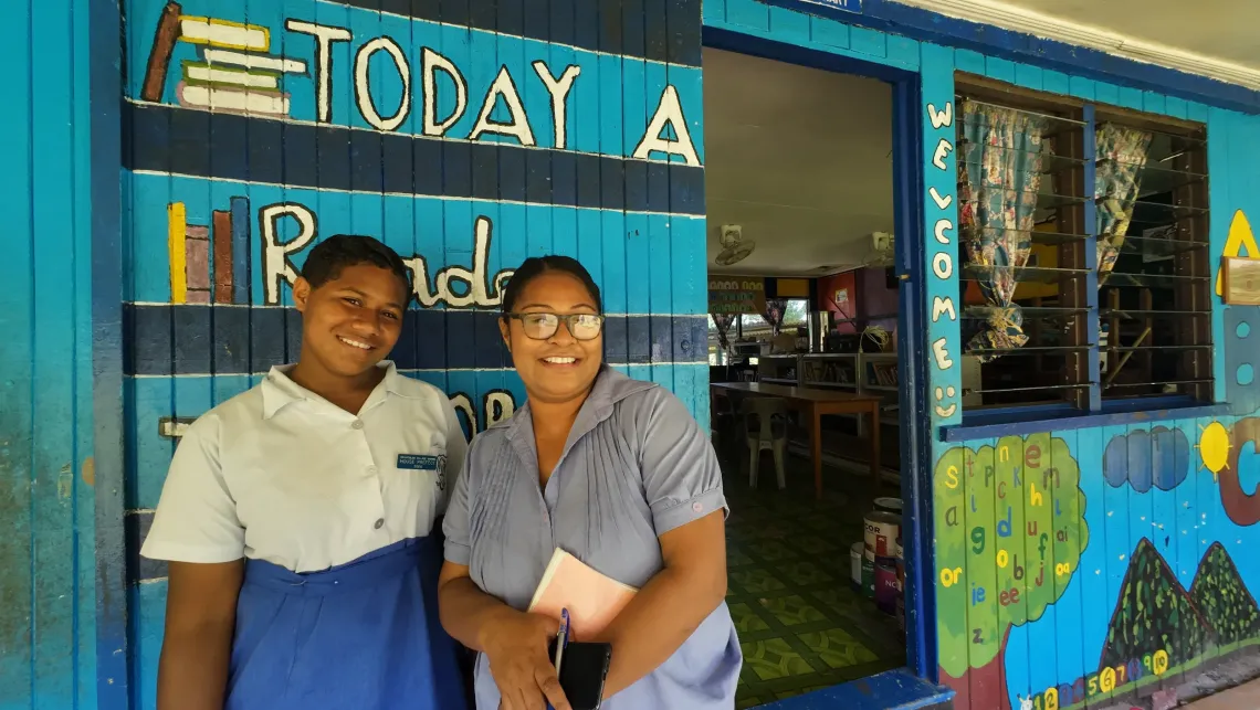 A teacher and student stand in front of a colourful, blue painted school corridor