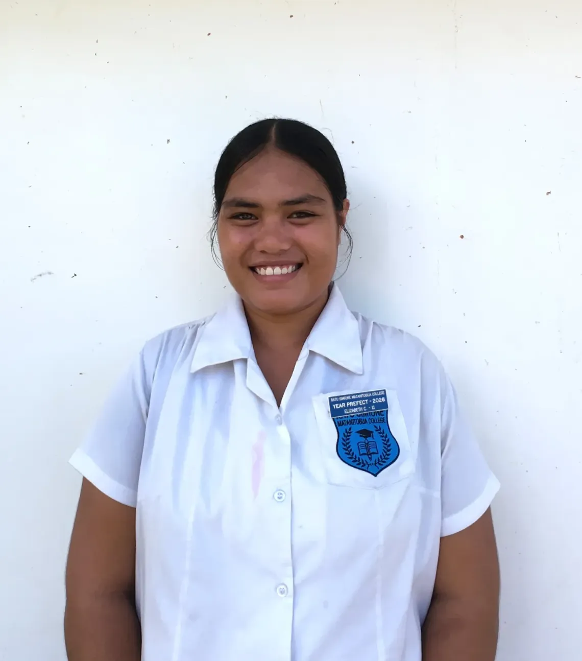 An adolescent school girl in Fiji smiles as she looks at the camera.