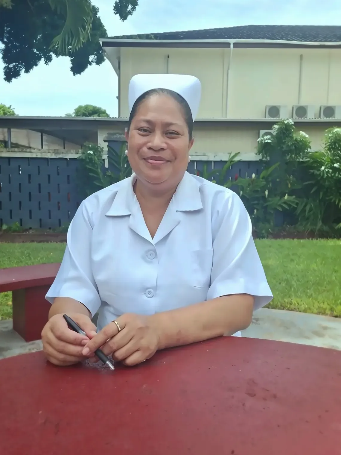 Nurse Sela sits at a red, outdoor table, smiling at the camera