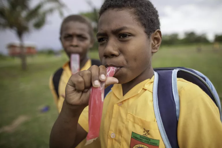 Oswin, 11, and Robert, 10, eat sugary ice sticks outside of their school in Guadalcanal, Solomon Islands.