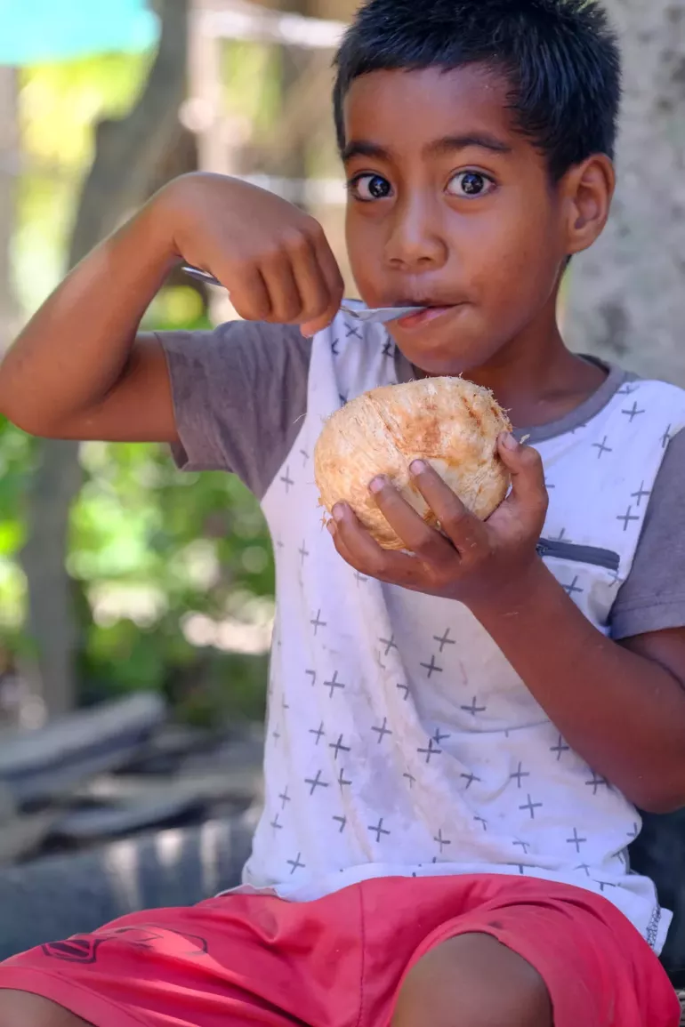 A child takes a nutritious break from playing with other children on Abatao Island in North Tarawa, Kiribati, while enjoying a coconut.