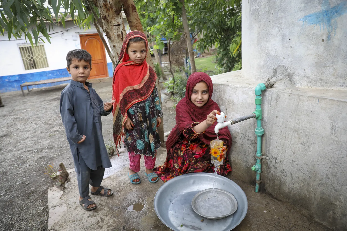 Khadija (right) and her siblings fill a glass of water from the water storage in their home which receives safe and abundant water from the UNICEF supported water source in their village, Bassu Mera.