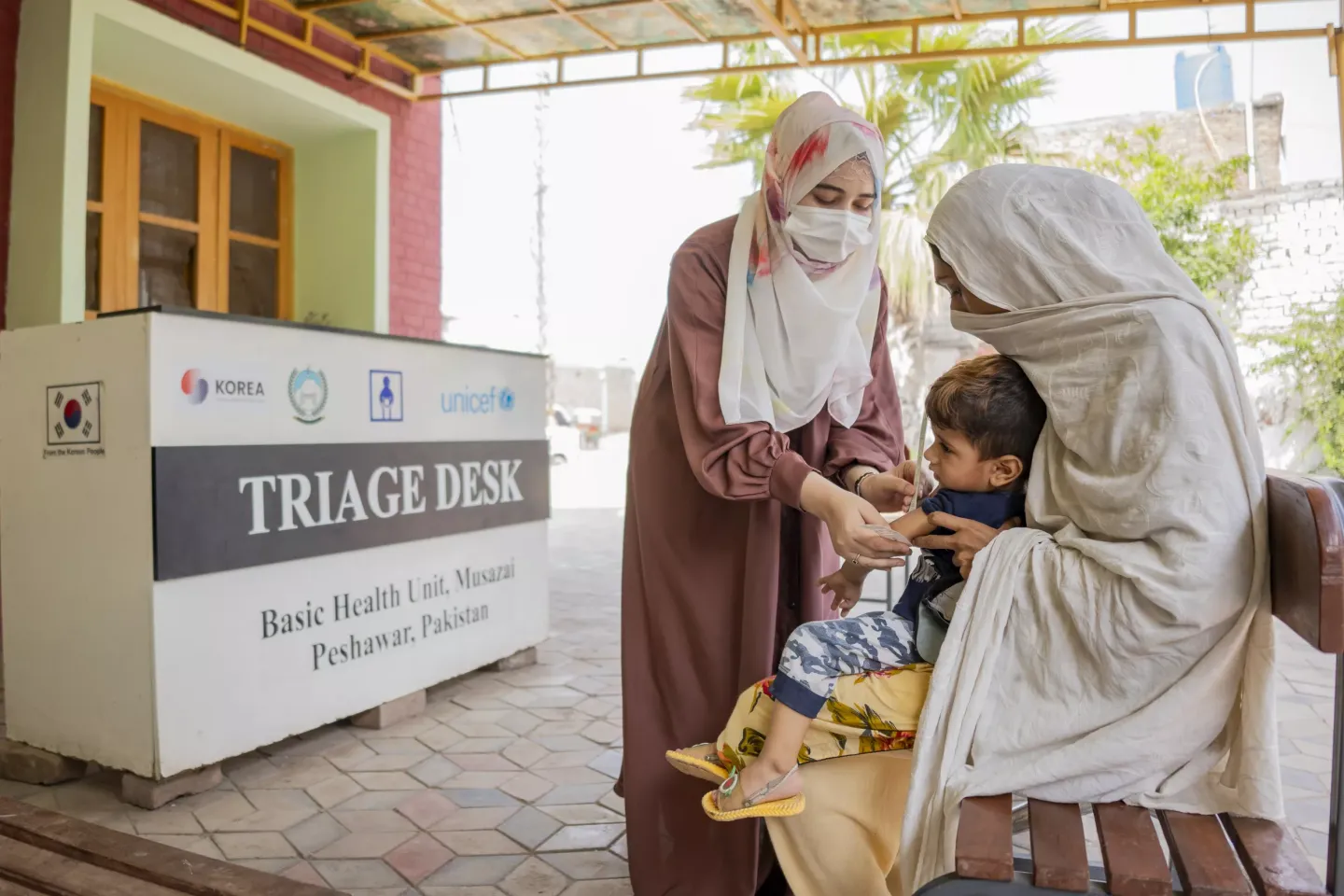 A lady health visitor at a newly established UNICEF-supported triage desk at a basic health centre in rural Pakistan checks a child who is in his mother's lap for nutrition status through the mid-upper arm circumference tape. 