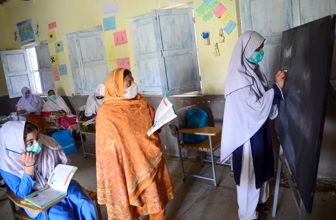 Girl writes on a blackboard while her teacher oversees the work in the Hangu area of the Khyber-Pa