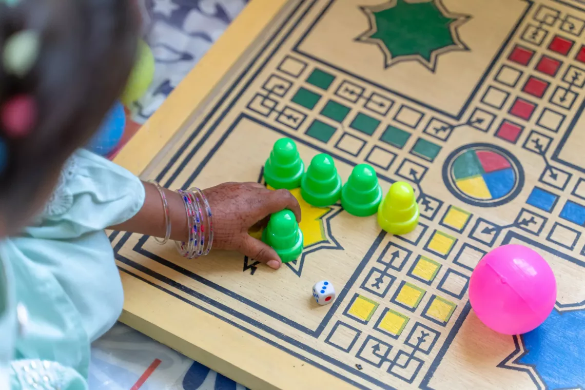 Infant girl plays a game of ludo at a child protection centre in Pakistan. The photo is a close-up of the ludo board with the child's tiny hand shown in action. Identity concealed for privacy and protection.