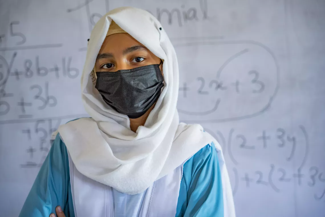 Kashaf (13) poses in front of the class board. 