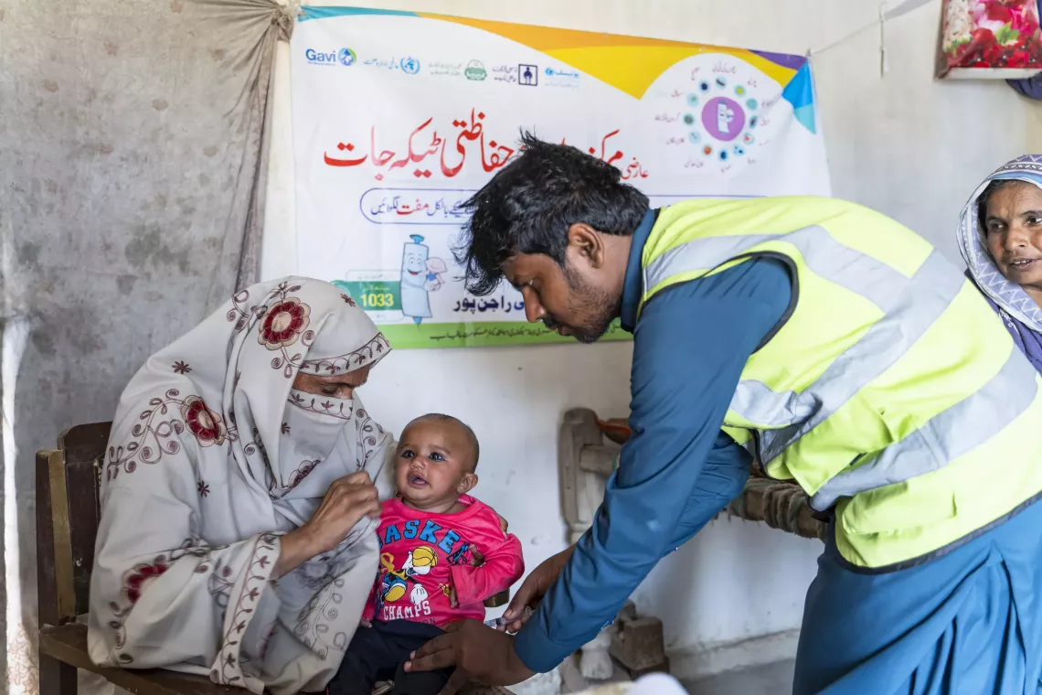 Vaccinator Adnan Haider (Right) is immunizing Hunsa (4 months) held by her mother Nasreen (Left), in a vaccination outreach Kit Station in the flood-affected village Basti Sahu, Rajanpur district, Punjab.