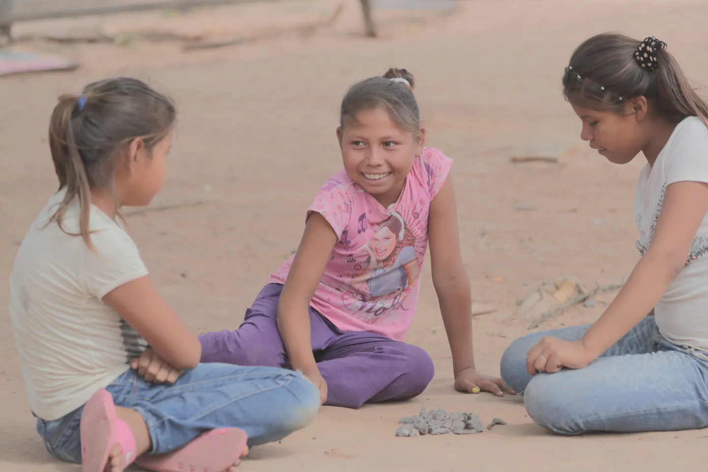 Tres ni&ntilde;as sentadas en el suelo jugando con piedritas