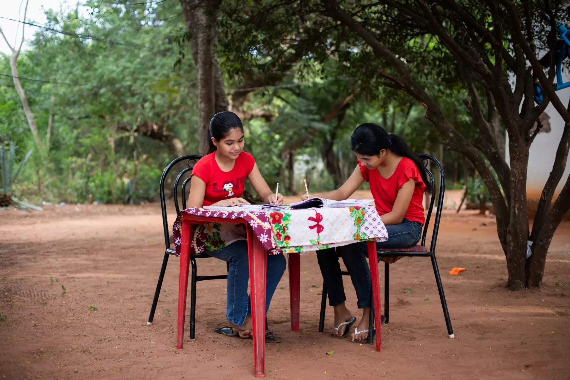 Dos ni&ntilde;as con remeras rojas realizan sus tareas escolares en una mesa ubicada en el patio