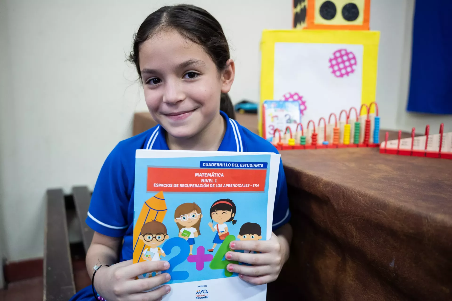 Ni&ntilde;a sonriendo sostiene un libro de tareas