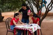 Dos ni&ntilde;as con remeras rojas realizan sus tareas escolares, en compa&ntilde;ia de su madre, en una mesa ubicada en el patio