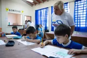 En un aula de clases, los ni&ntilde;os est&aacute;n realizando tareas, la maestra observa y los ayuda.