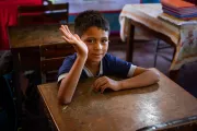Ni&ntilde;o saludando sentando en un aula de clases