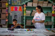Ni&ntilde;o aprendiendo con materiales did&aacute;cticos junto a su maestra en un aula decorada y colorida.