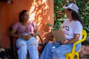 Una facilitadora social con una planilla en la mano sentada al lado de la madre de Daiver, conversan.