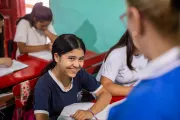 Una ni&ntilde;a sentada en el salon de clases, sonriendo a su maestra