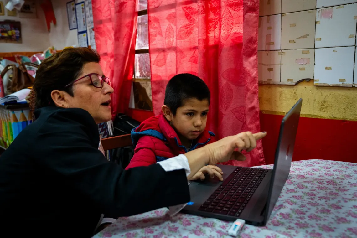 Docente y estudiante utilizan una computadora port&aacute;til durante una actividad de aprendizaje en un entorno educativo.